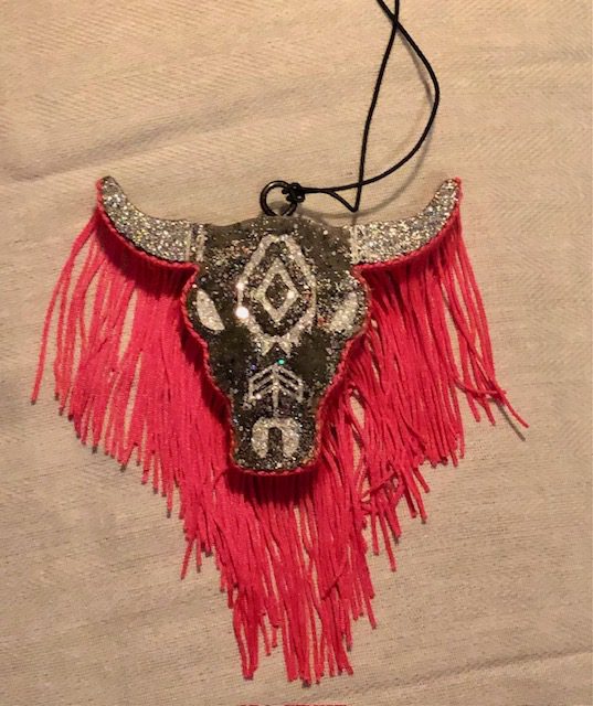 A red PINK COW SKULL FRESHIE with fringes hanging from a necklace.