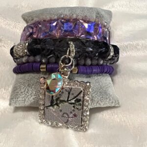 A purple and black PINK UPCYCLED BRACELET with a charm on it.