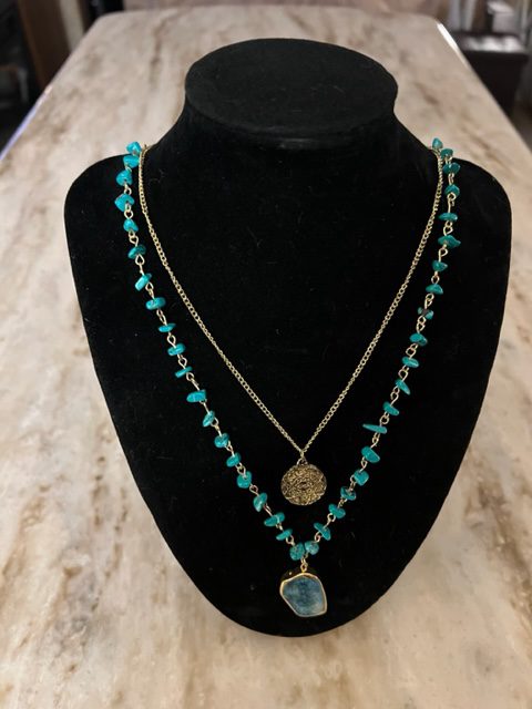 A trailblazer necklace with turquoise beads and a gold coin.