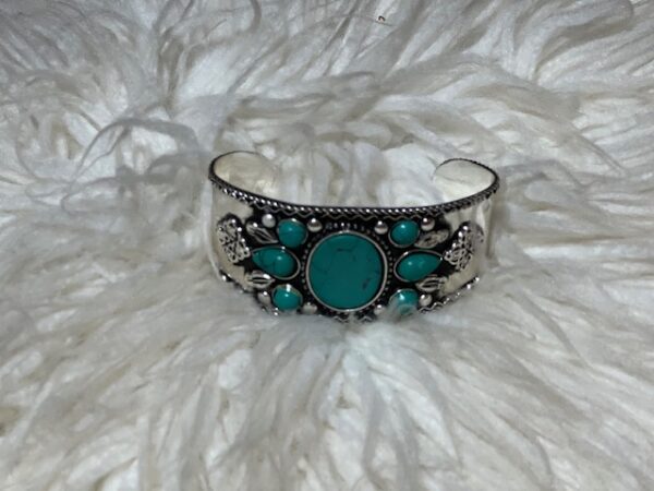 A silver bracelet with turquoise stones on top of white fur.