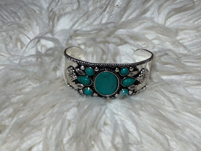 A silver bracelet with turquoise stones on top of white fur.