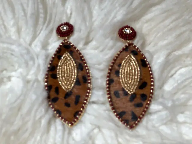 A pair of leopard print earrings on top of white fur.