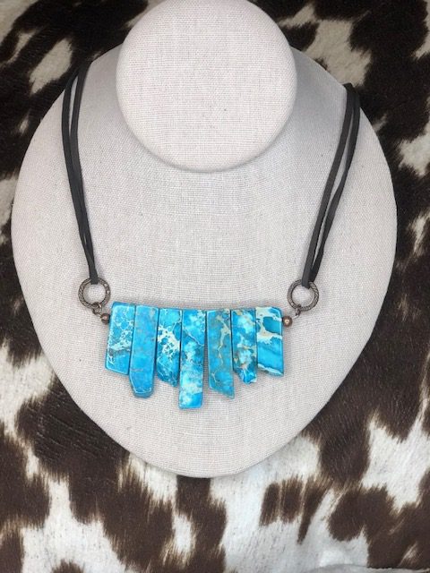 A Jasper slab necklace with turquoise stones on a cowhide.