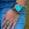 A woman wearing a bracelet with a turquoise stone and LEOPARD LEATHER CUFF.
