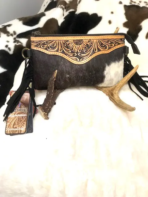 A HAIR ON HIDE TOOLED FRINGE CLUTCH with tassels sitting on a bed.