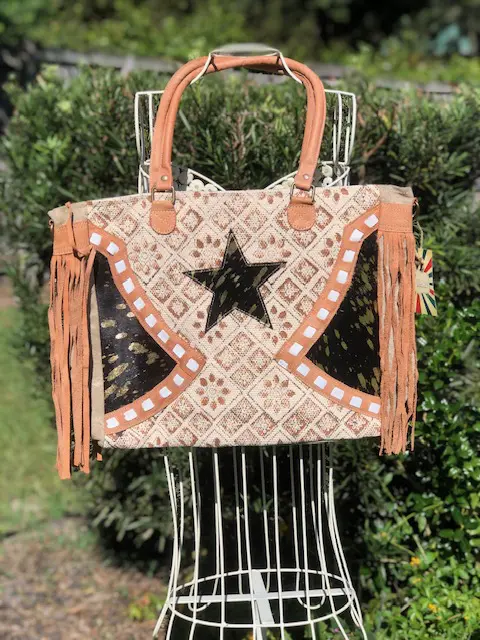 A COWHIDE LEATHER AND UPCYCLED CANVAS WEEKENDER with fringes and a star on it.
