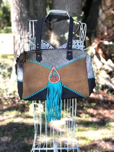 A TURQUOISE FRINGE LADIES BAG with tassels hanging on a chair in the woods.