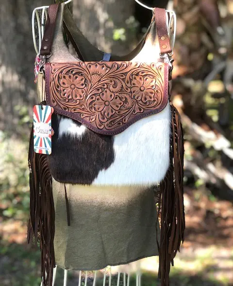 A TOOLED FRINGED HAIR ON HIDE PURSE with fringes hanging on a mannequin.
