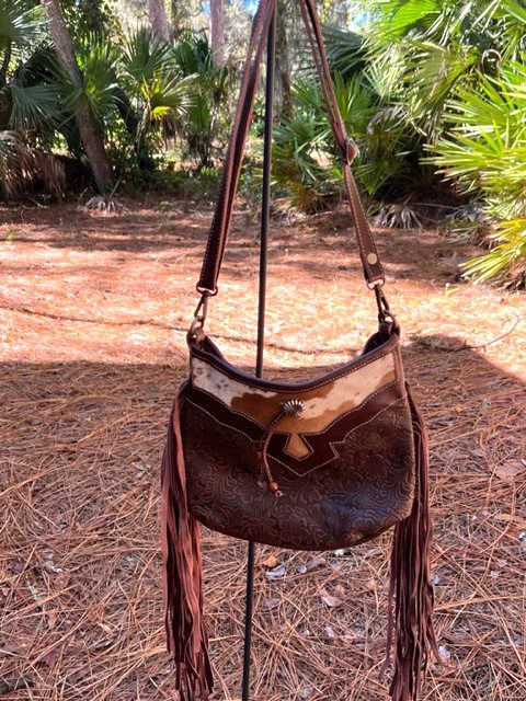 A SCULPTED BROWN LEATHER & HAIR ON BAG hanging on a pole in the woods.