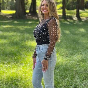 A woman standing in the grass wearing a SHEAR PEARL BEADED MESH TOP IN BLACK and jeans.