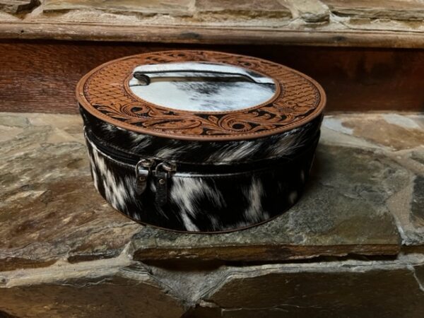 A black and white WESTERN MESA ROUND HAND TOOLED JEWERLY BOX sitting on a stone floor.